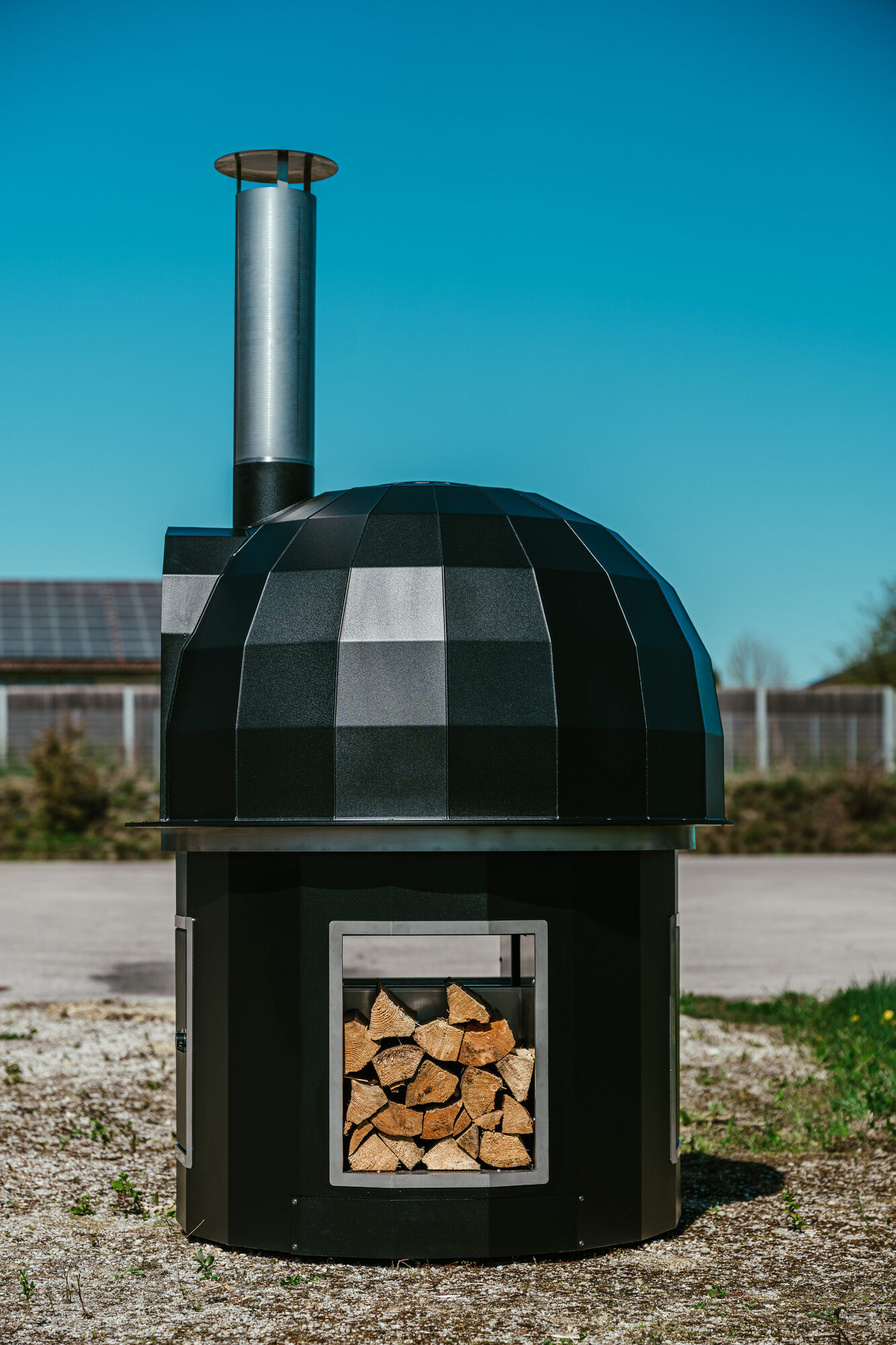 Schwarzer THOLOS Holzbackofen mit Brennholz im Staufach